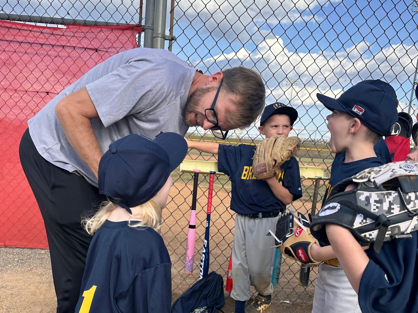 Coach Mark leaning down to talk with a young player at the dugout